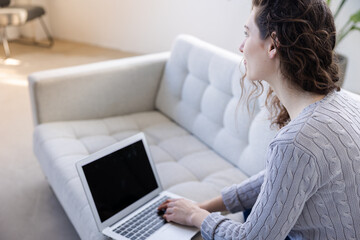 Fototapeta premium Woman sit in a sofa with her laptop with a smile on her face in her apartment view over her shoulder
