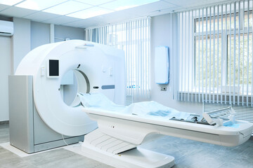 Modern large computer tomography machine with table covered with disposable sheet in hospital room