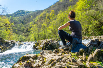 Naklejka premium A young woman sitting on the Sella river between the Tornin a la Olla de San Vicente, near Cangas de Onis. Asturias. Spain