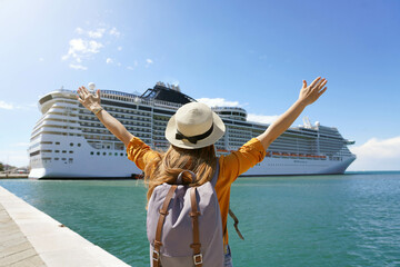 Back view of traveler girl with raised arms standing in front of big cruise liner - obrazy, fototapety, plakaty