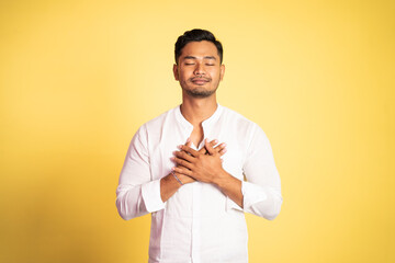 young handsome man wearing white shirt holding chest and closing eyes feeling peace serenity on...