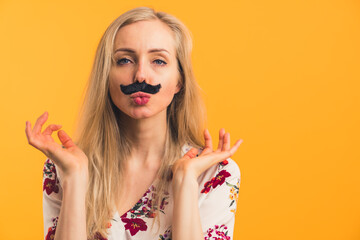 Portrait young blond Caucasian woman having fake mustache on her face, kissing gesture isolated orange background copy space indoors . High quality photo