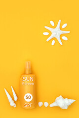 Suntan protection sunscreen bottle UV factor 50 for safe anti cancer skincare sunbathing concept with abstract starfish sun and decorative sea shells. Top View, flat lay, copy space on yellow.