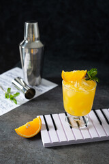 Refreshing Vodka OJ Screwdriver Cocktail. Homemade orange cocktail with mint and vodka on dark background with bar tools. Rum with orange juice.