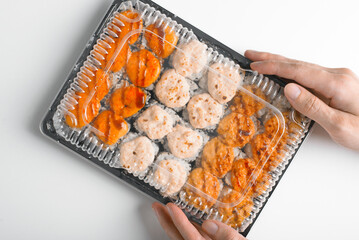 Delivery of Japanese traditional sea food, Asian cuisine. Close-up of hand holding set of hot baked yaki maki rolls in plastic box, top view