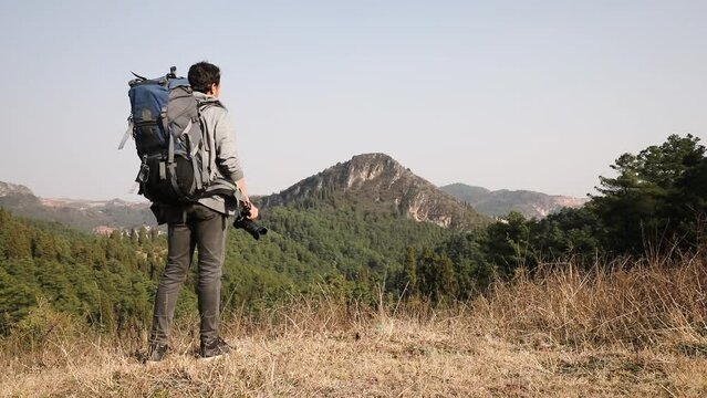 Man hikes with his backpack and takes a picture of the landscape with a camera