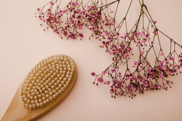 Dry wooden anti cellulite brush for self home massage near a purple gypsophila on a pink background. Spa concept