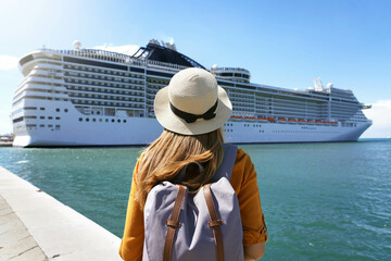 Cruise vacation. Rear view of tourist girl with backpack and hat standing in front of big cruise ship. - obrazy, fototapety, plakaty
