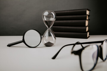 Fototapeta na wymiar Hourglass with glasses, magnifier and books on a table