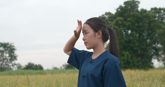 Portrait of Tired Asian young farmer woman wiping sweat from forehead with hand in the paddy field.