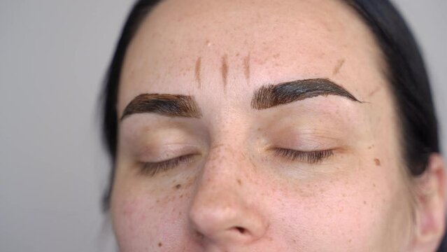 gloved hands apply henna to dyed eyebrows with a brush