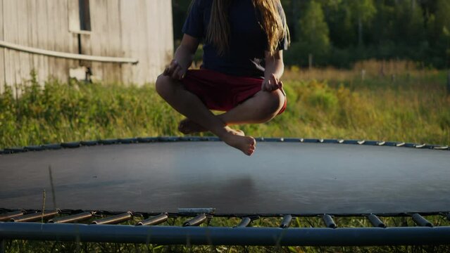 Closeup of a kid springing in slowmotion on a trampoline while in a lotus position.