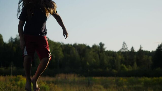 Camera pan of a kid jumping and flailing around in front of barn and field.