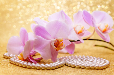 purple Orchid and pearl necklace on a shiny gold background
