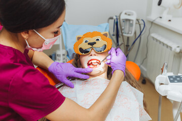 dentist using a rubber dam while examining a patient. little girl with a cheek retractor in her...