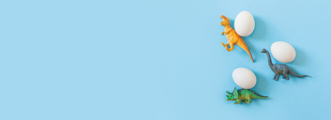 Easter egg hunt holiday composition, white eggs with coloful dinosaur on light pastel blue backgroind. Seasonal spring kids game concept. Flat lay, minimal, trendy, top view, place for text, banner