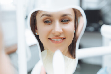 A young woman patient looks at her teeth in the mirror. Modern dental clinic. teeth whitening