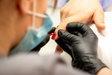 Manicure varnish painting. Close-up of a manicure master wearing rubber black gloves applying red varnish on a female fingernail in the beauty salon