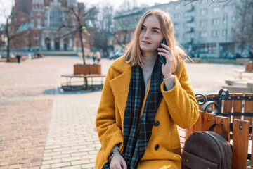 Fototapeta premium Beautiful smiling 30s woman with mobile phone walking on the street. Female calls by smart phone