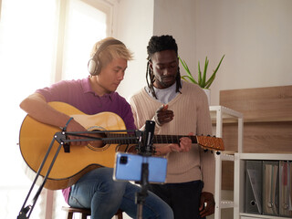 A personal afroamerican tutor explains to his asian student how to play studied chord correctly....