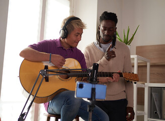 A personal afroamerican tutor explains to his asian student how to play studied chord correctly. Musical education at home