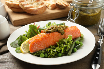 Tasty cooked salmon with pesto sauce and fresh salad served on wooden table, closeup