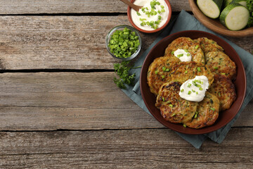 Delicious zucchini pancakes with sour cream served on wooden table, flat lay. Space for text