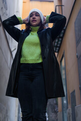 low angle shot of a pretty young woman dressed in winter clothes with her arms raised who is on an alley looking away