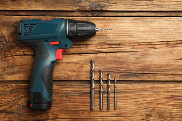 Modern electric power drill with twist bits on wooden table, flat lay. Space for text