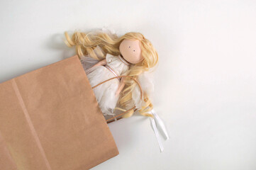 Brown transparent empty paper bag with a beautiful handmade doll in the form of a white angel. White background.