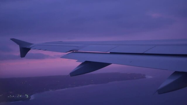 View from illuminator on airplane wing over the water at sunset. 4K, Gaining altitude, Handheld