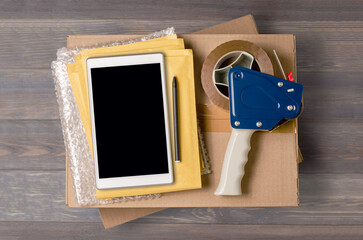 Cardboard box, smartphone, bubble wrap and packaging tools. The concept of packaging parcels for an online store. View from above. Brown wooden background