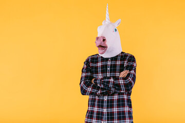 Person dressed in unicorn mask with plaid shirt and crossed arms, on yellow background. © Davidbenito