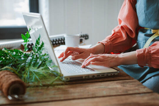 Fashionable stylish girl hipster florist in a work apron working at a laptop, looking at a smartphone check online stores for sales cyber monday technology - Powered by Adobe