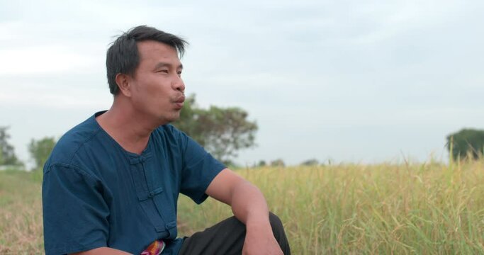 Portrait shot of Happy Asian farmer man in a blue dress whistling at the paddy field.