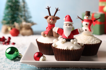 Different beautiful Christmas cupcakes on blue table with festive decor and snow