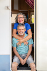 vertical portrait of a retired couple smiling and looking at the camera next to their motorhome