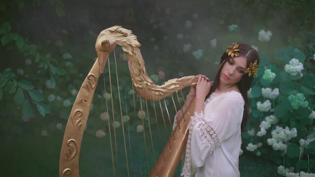 Fantasy woman greek goddess muse holding in hands musical golden instrument vintage ancient golden harp. Girl elf princess forest nymph. Summer nature, green grass trees. White dress gold crown wreath