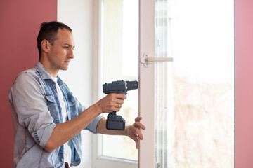 Handyman using a cordless screwdriver to install a window handle. Qualified worker services, home repair and renovation.