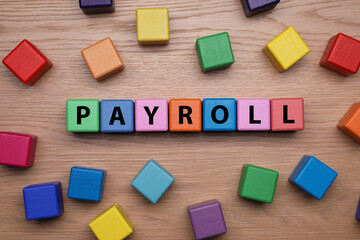 Colorful cubes with word Payroll on wooden table, flat lay