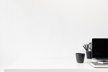 Office table, empty desk with laptop, mobile supplies and white wall copy space.	
