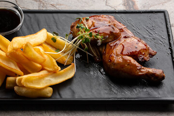 Grilled quail carcass with french fries on plate over black stone background. Roasted quails on...