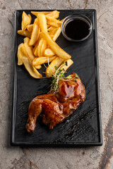 Grilled quail carcass with french fries on plate over black stone background. Roasted quails on...