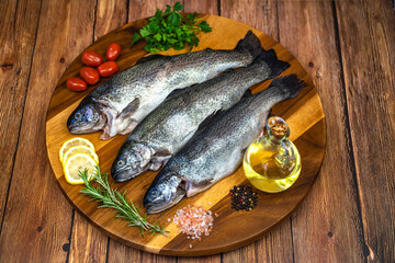 Three raw trout with spices and olive oil on a wooden board.