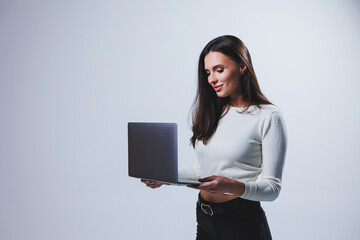 Young woman manager in a white shirt holds a portable laptop in her hands while standing on a gray background