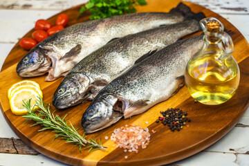 Three raw trout with spices and olive oil on a wooden board.