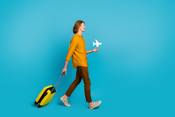 Full size profile side photo of man leaving on weekend travel go with luggage hold plane card isolated on blue color background