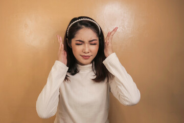 Portrait of young asian woman isolated on orange background suffering from severe headache,...