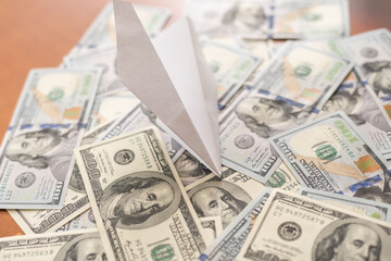 origami airplane lands on a pile of banknotes from the US dollar.