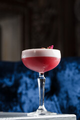 Pink Clover Club Cocktail in Coupe Glass with Layer of Foam and flower Garnish isolated on dark...